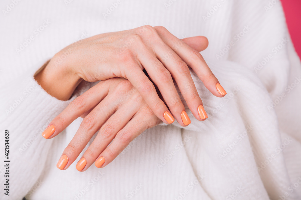 close frame of woman's hands with orange manicure on white sweater and pink background isolated copy space close frame of woman's hands with orange manicure on white sweater and pink background isolated copy space
