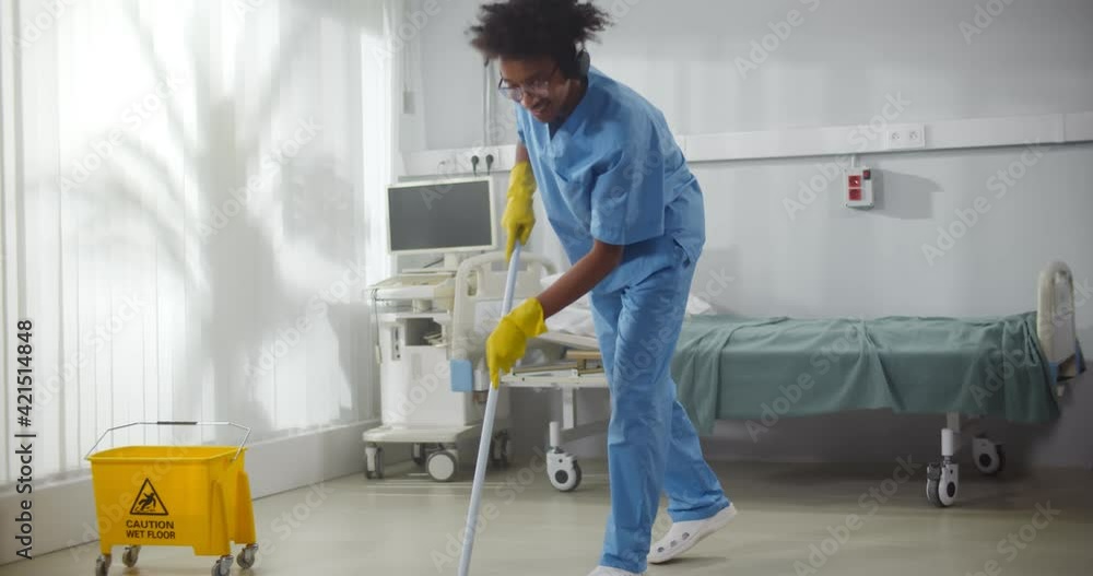 Afro-american male janitor in headphones washing floor in hospital ward Afro-american male janitor in headphones washing floor in hospital ward