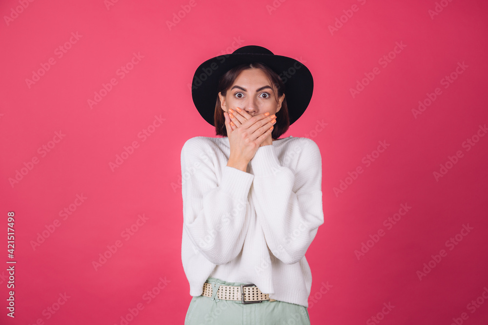 Stylish woman in white casual sweater and hat on red pink background copy space shocked look to camera cover mouth with hands Stylish woman in white casual sweater and hat on red pink background copy space shocked look to camera cover mouth with hands
