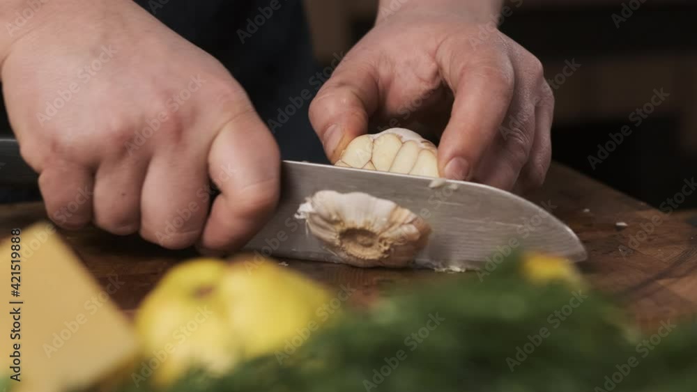 chef in restaurant kitchen cuts garlic with sharp, shiny knife. man prepares food for family and cuts garlic on wooden cutting board. chef in restaurant kitchen cuts garlic with sharp, shiny knife. man prepares food for family and cuts garlic on wooden cutting board.