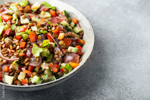 salad with lentils and vegetables in a deep plate on a dark gray background, vegetarian food