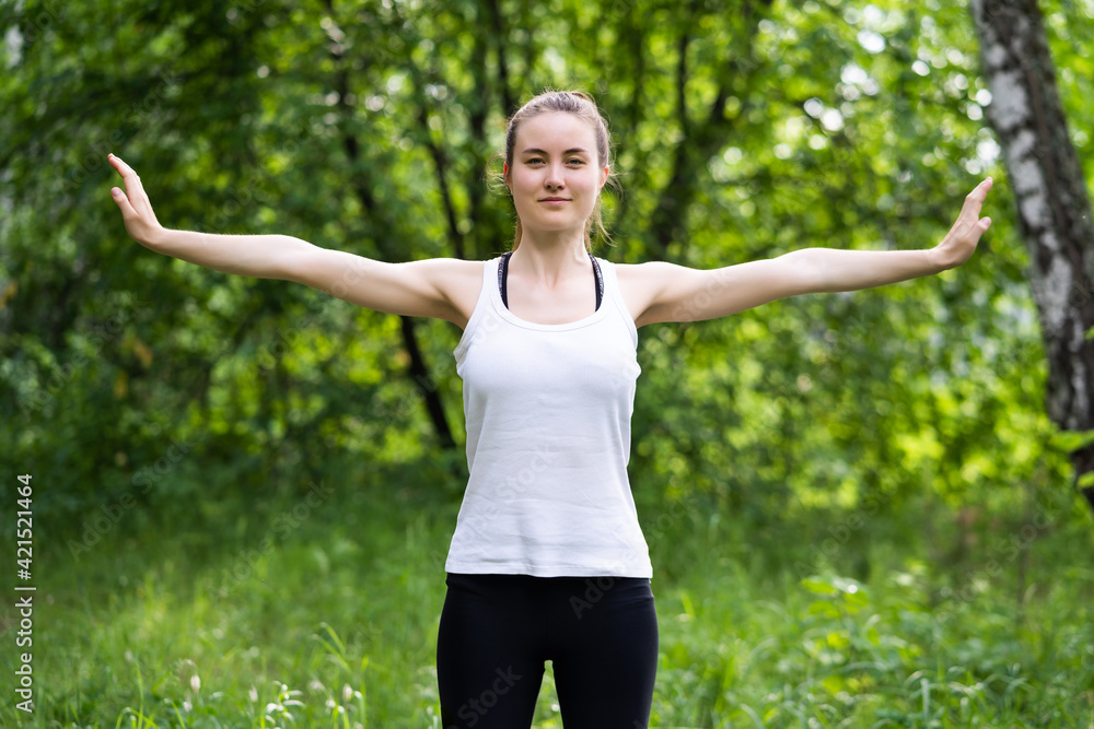Fit young beautiful woman wearing white top and black sporty leggings working out outdoors in park on summer day Fit young beautiful woman wearing white top and black sporty leggings working out outdoors in park on summer day