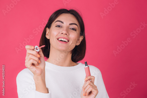 Stylish woman in casual white sweater on pink red background isolated space happy positive hold lipstick