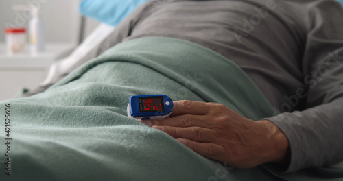Close up of patient lying in hospital bed wearing pulse oximeter to measure blood oxygen saturation