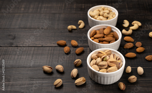 Almonds with cashews and pistachios in white ceramic cups on a dark wooden background. Copy space, no people, flatlay