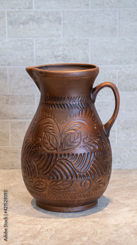 An earthenware jug with a beautiful floral ornament on the kitchen table. Pottery, jug, earthenware. 