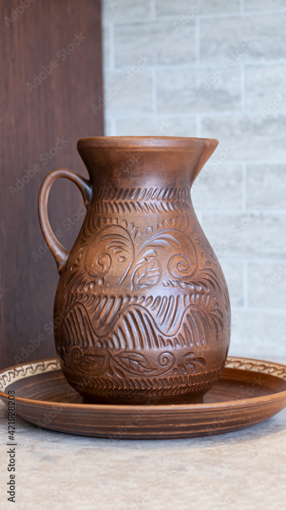 An earthenware jug with a beautiful floral ornament on the background of a wooden kitchen made of solid oak. Pottery, jug, earthenware. 