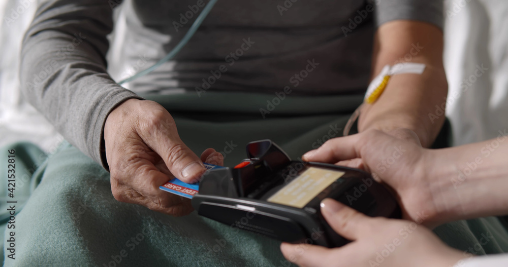 Male patient with intravenous drip using credit card paying for health insurance in hospital ward Male patient with intravenous drip using credit card paying for health insurance in hospital ward