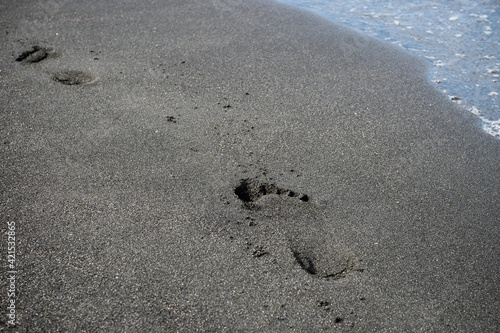 foot prints on a black sand beach with tilt-shift blur. Surf in background.