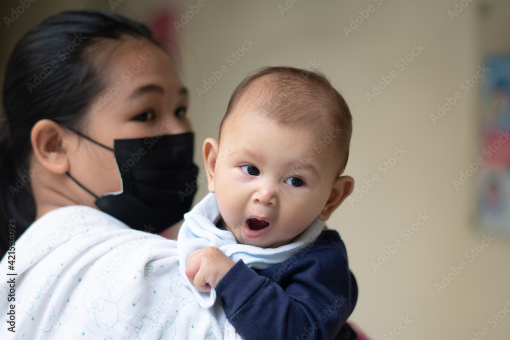 Asian Baby Girl Yawning while being held by mother wearing a mask during pandemic Asian Baby Girl Yawning while being held by mother wearing a mask during pandemic