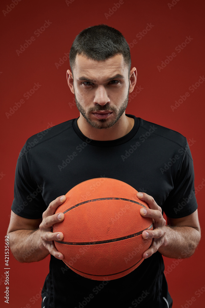 Seriously basketball player holding with both hands a orange ball