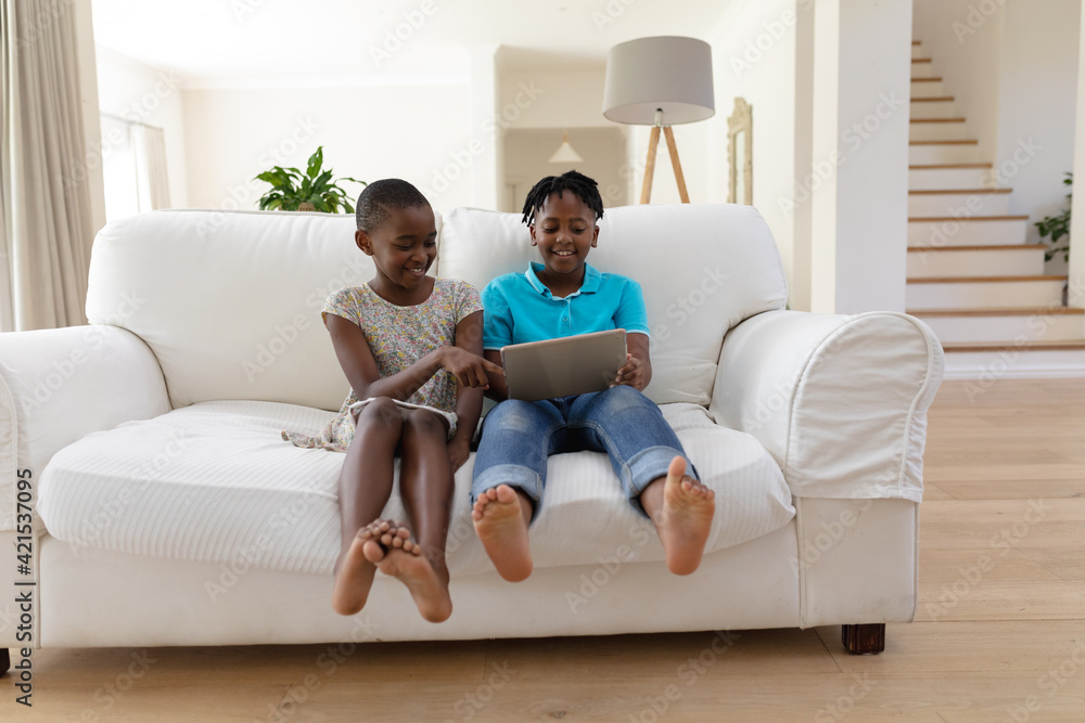Smiling african american brother and sister sitting on couch using digital tablet