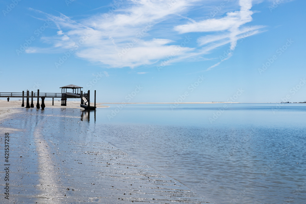 Boat pier at the estuary of Tybee Creek and the Atlantic ocean, blue sky with clouds reflected in the still waters, horizontal aspect