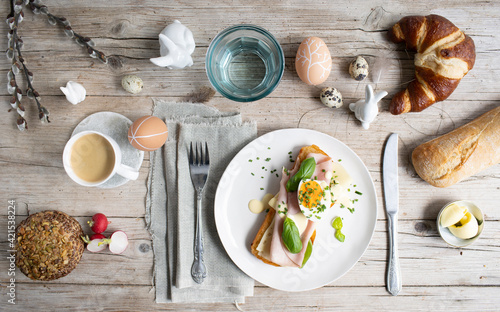 Easter breakfast with golden toasted Easter bread with butter and cheese and ham with egg and chives and basil with Easter decoration on light wooden background and various pastries