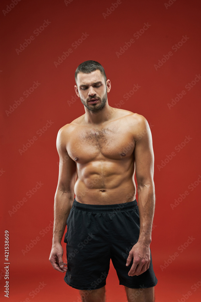 Strong athlete posing at the photo camera in black sportswear isolated on red background