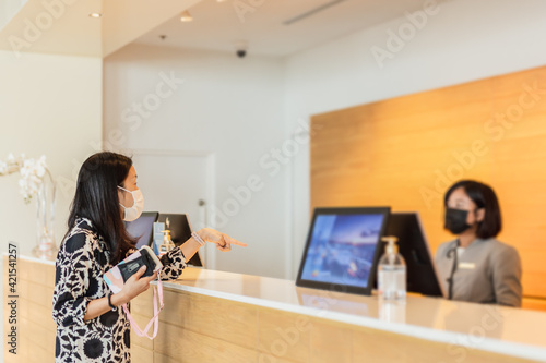 Canvas Print Woman hotel guest and receptionist at hotel counter wearing medical mask against virus