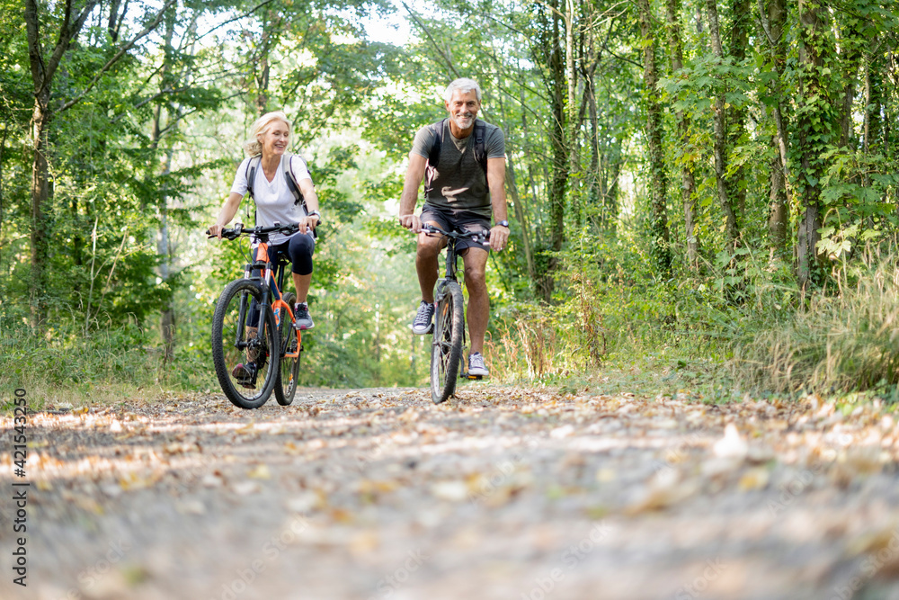 Smiling mature couple riding bicycles in forest Smiling mature couple riding bicycles in forest