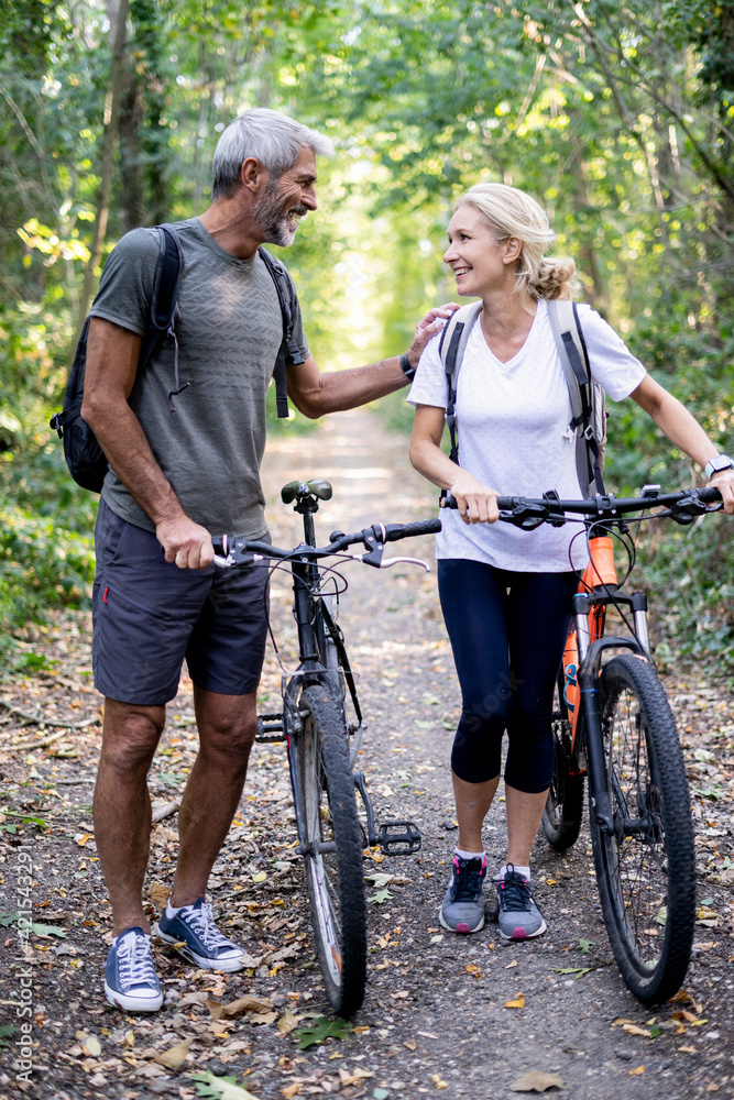 Smiling mature couple with bicycles walking on footpath in forest Smiling mature couple with bicycles walking on footpath in forest