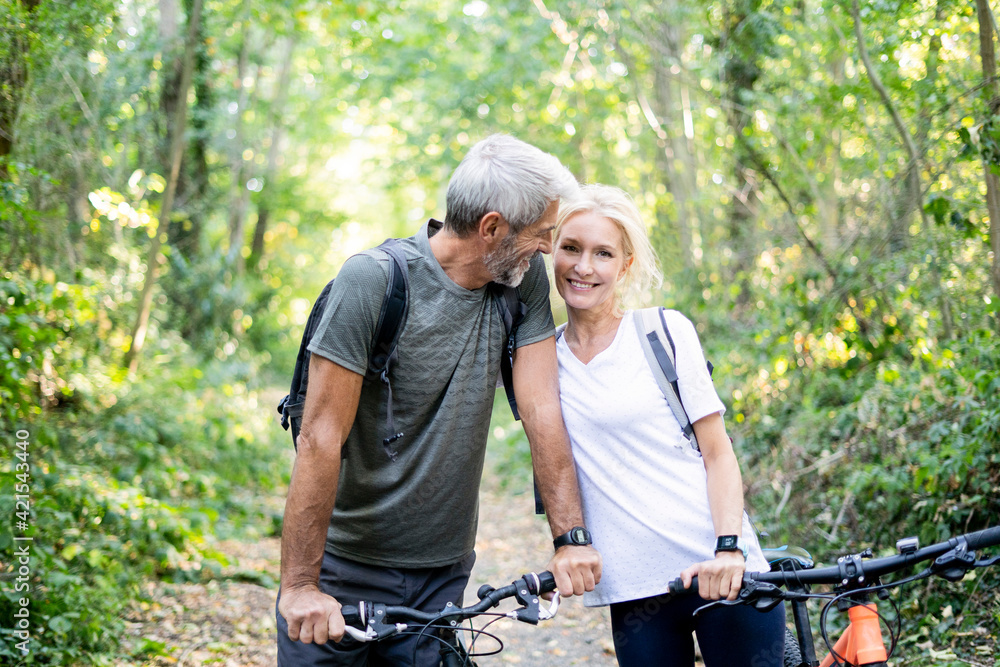 Smiling mature couple with bicycles standing in forest Smiling mature couple with bicycles standing in forest