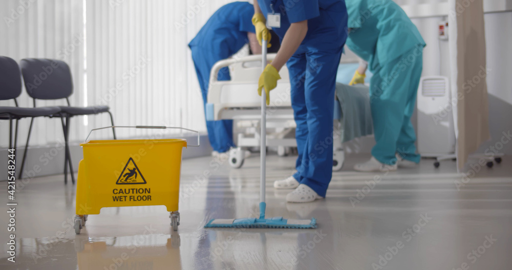 Nurses mopping floor and making bed in empty hospital ward Nurses mopping floor and making bed in empty hospital ward