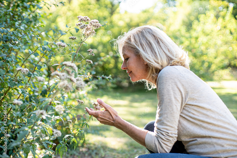Smiling mature woman looking at flowers in backyard Smiling mature woman looking at flowers in backyard
