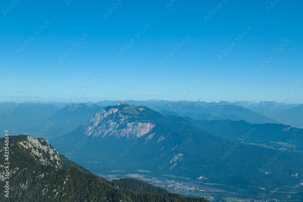 A panoramic view on the Alps from the top of Mittagskogel in Austria. Clear and sunny day. Sharp peaks around. A bit of haze in the valley. Outdoor activity. Lush green slopes with barren peaks. Calm
