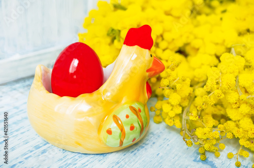 Easter composition. A red painted egg in a ceramic chicken with a bouquet of spring yellow mimosa on the Easter table