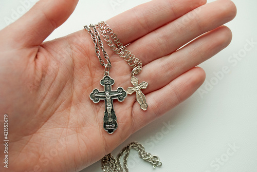 Two silver crosses in a female hand on a white background. Male and female Christian cross.