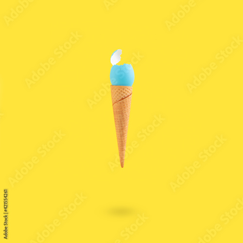 Creative Easter concept with blue color eggshell in ice cream cone on yellow background