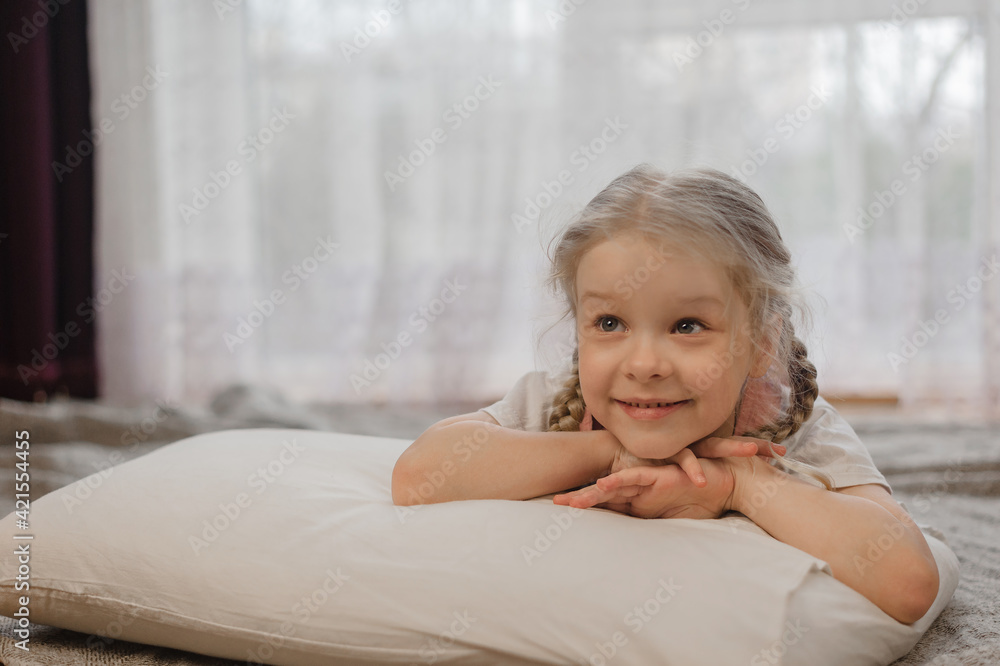 a little girl with two pigtails of blond hair lies on her stomach on the floor of the house and shows her tongue a little girl with two pigtails of blond hair lies on her stomach on the floor of the house and shows her tongue