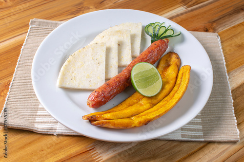 Arepa with chorizo, fried banana, lemon, traditional Colombian food, on wooden background
