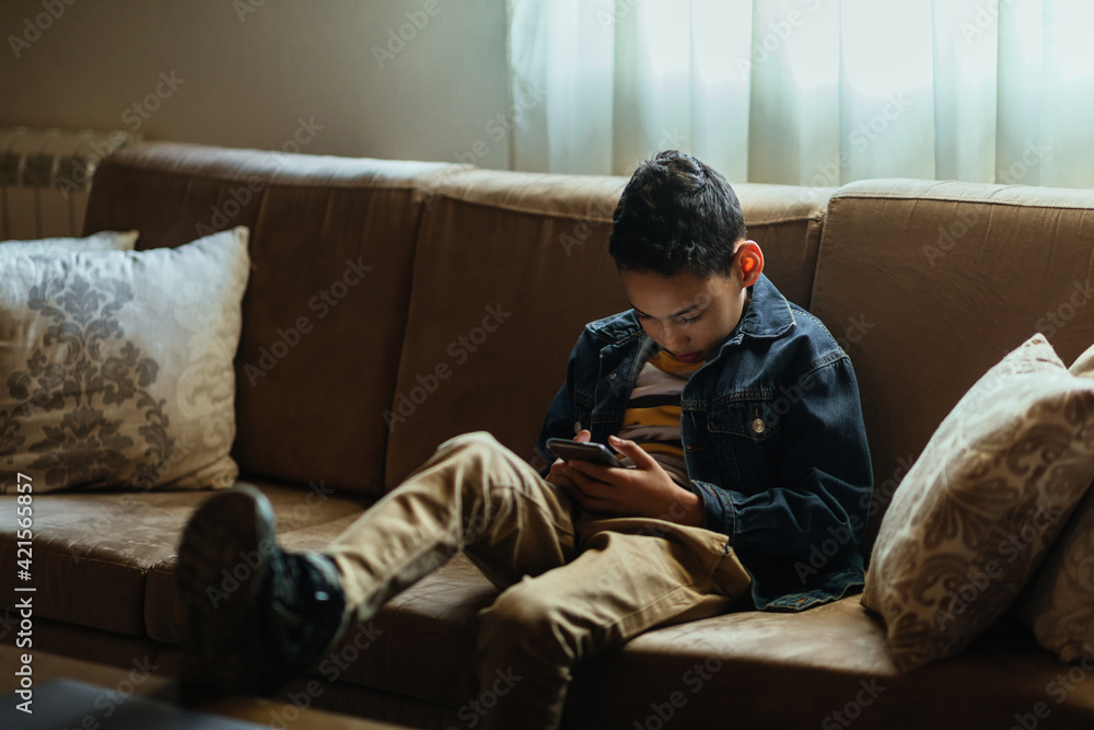 Little black boy sitting on sofa and using phone