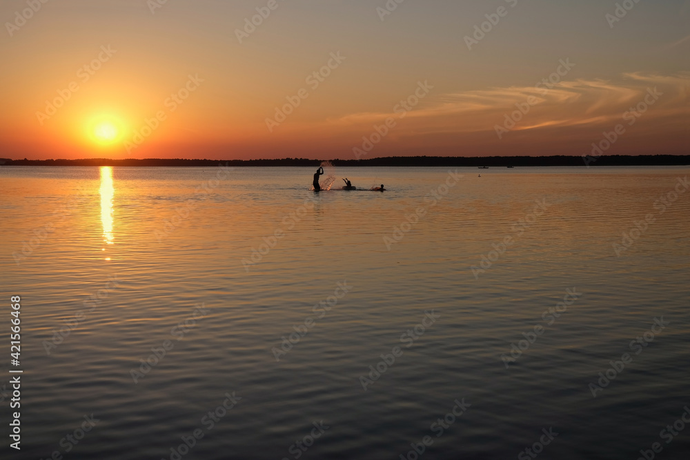 Happy family resting on the lake. Make splashes of water around. Human silhouettes on sunset background. Lake Svityaz, Ukraine. Copy space. 