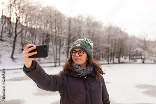 woman in winter clothes taking a selfie by the frozen lake in winter, snowy day
