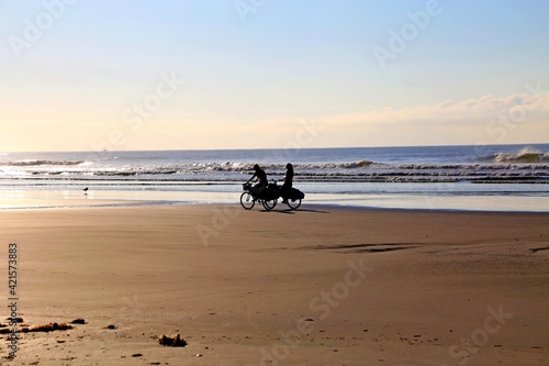 Two girls friends riding bicycles in the beach sand at the sunset. Surf boards, sand and waves. 