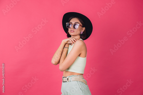 Beautiful stylish woman in hat and sunglasses posing over pink red background, isolated copy space © Анастасия Каргаполов