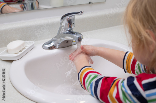 Child washing hands with soap in the bashroom photo