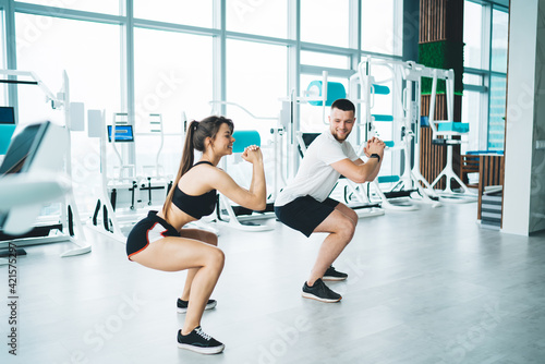 Fit smiling sportspeople squatting on floor in modern gym