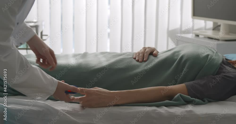Doctor examining patient with fingertip pulse oximeter in hospital bed Doctor examining patient with fingertip pulse oximeter in hospital bed