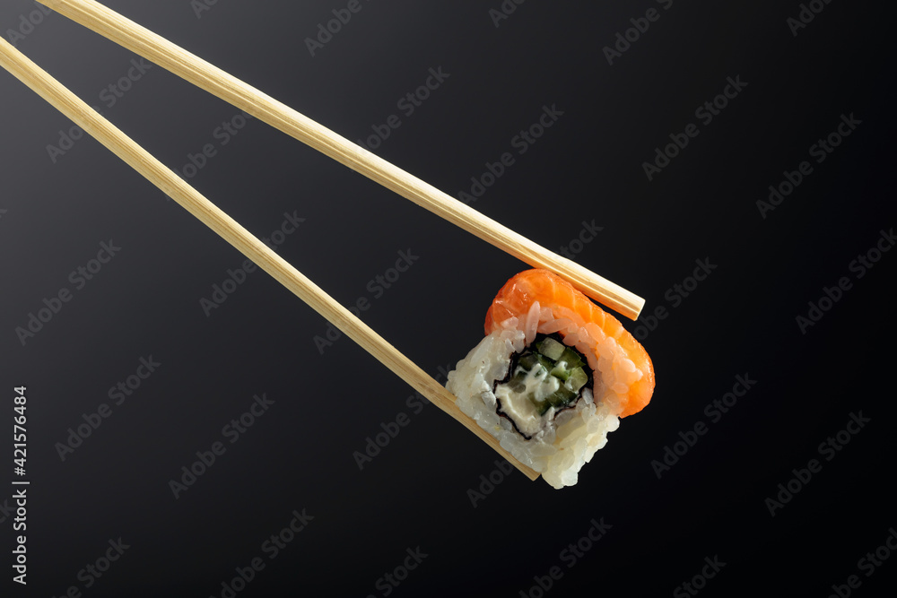 Fresh tasty sushi with salmon in wooden chopsticks on a dark background. Fresh tasty sushi with salmon in wooden chopsticks on a dark background.
