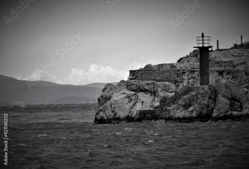 Lighthouse by the sea on a big cliff and waves black and white