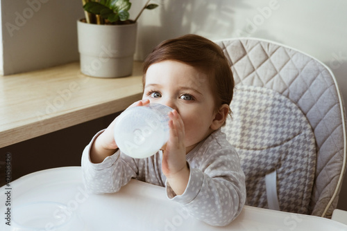 Lovely baby boy age of 1 year drinking milk from a small bottle, kids breakfast food