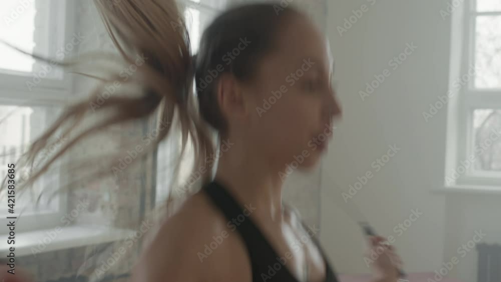 Slow-motion medium closeup of attractive young fit woman doing cardio exercise with skipping rope training at loft style gym studio filled with chalk powder smoke Slow-motion medium closeup of attractive young fit woman doing cardio exercise with skipping rope training at loft style gym studio filled with chalk powder smoke