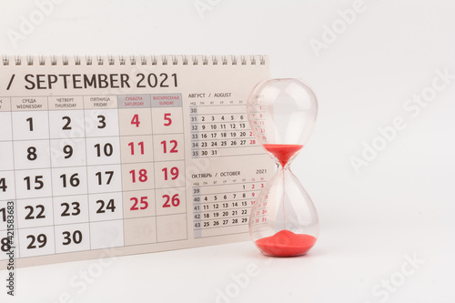 Time passing concept. Crystal hourglass with red sand and calendar on light background