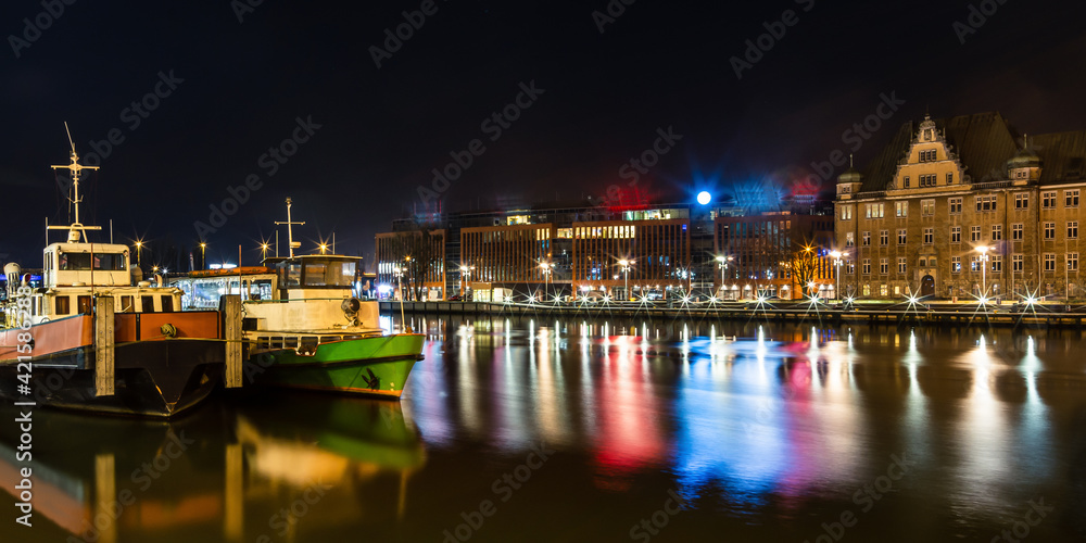 ships on the river with reflections of lights, in the background an old building and a new office building 
