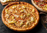 Tasty pizza with chicken meat, cheese, slices of pineapple, sauce and herbs on stone black background. Fast food lunch for picnic company, top view