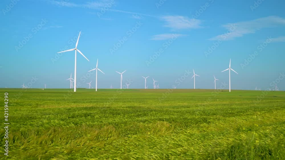Green wheat field in motion with wind turbines in the background. Wind Farm Turbines in wheat field. Aeolian generators in a beautiful wheat field. Aeolian turbine farm. Wind turbine. Wind energy Green wheat field in motion with wind turbines in the background. Wind Farm Turbines in wheat field. Aeolian generators in a beautiful wheat field. Aeolian turbine farm. Wind turbine. Wind energy
