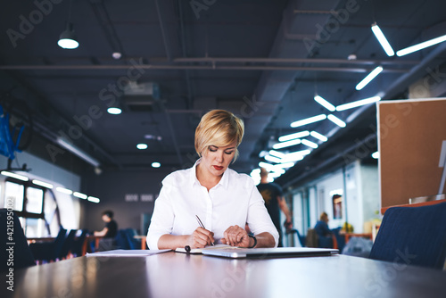 Thoughtful woman manager taking notes in office