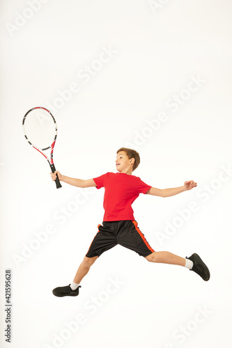 Adorable boy with tennis racket jumping in studio