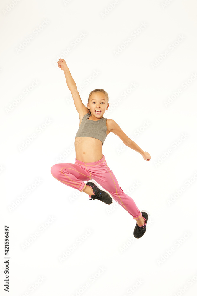 Cute female child in sportswear jumping in studio
